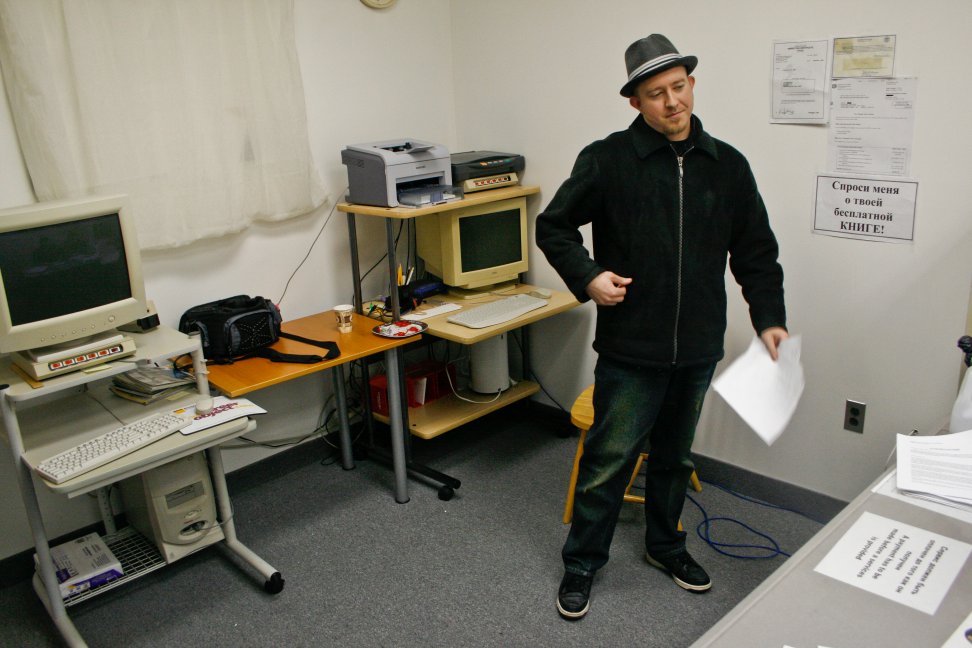A man wearing a fedora stands in an office holding audition pages.