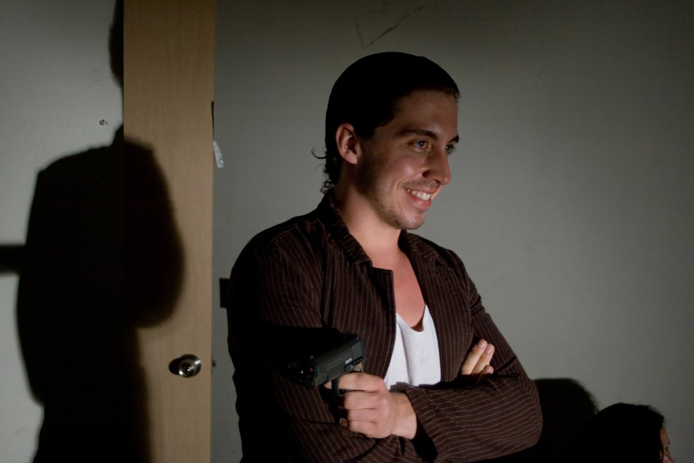 A smiling performer in a pinstripe jacket holds a prop pistol during a rehearsal.