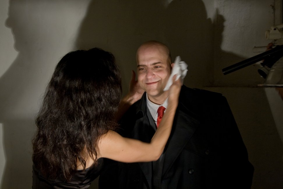 A makeup artist applies powder to a performer in a suit and red tie.