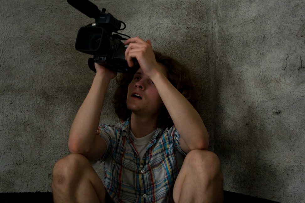 A seated camera operator raises a camcorder to frame a low-angle shot.