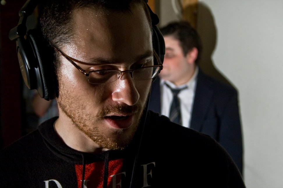 A crew member wearing headphones listens closely while a performer waits in the background.