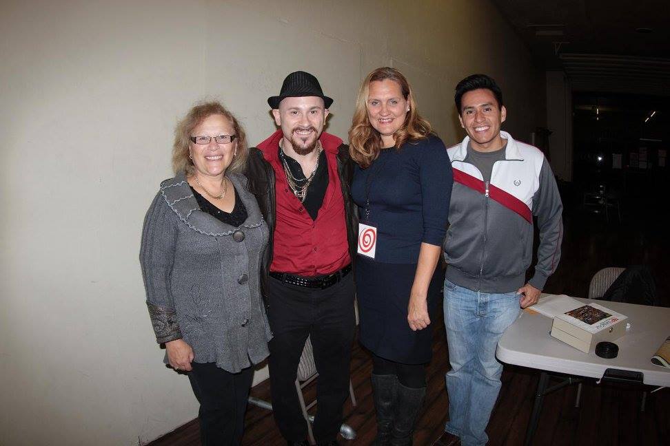 Four people smile together beside a table at a film event.